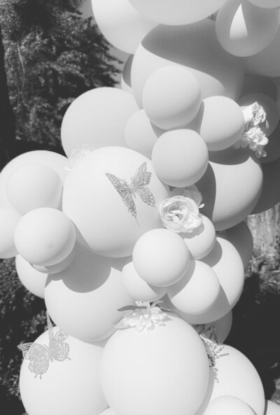 Black and white close-up photo of a custom balloon arch with flowers and butterflies