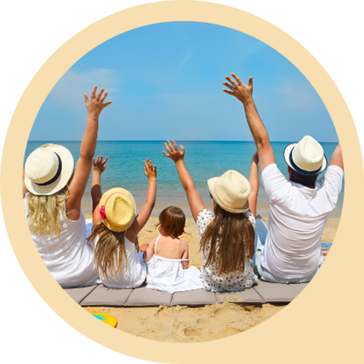 A young family sits on the beach, facing away from the camera and looking out at the crystal clear water: mother, father, and three young girls. They have their hands raised to the sky in celebration.