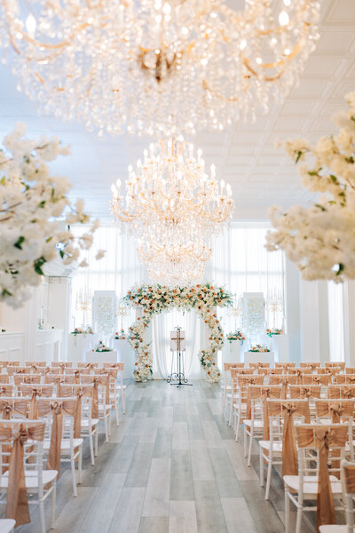 a luxury wedding ceremony is set in a ballroom with florals and chandeliers