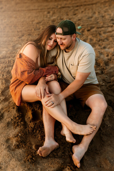 Couple snuggles each other on beach during family photo session by Overland Park photographers.