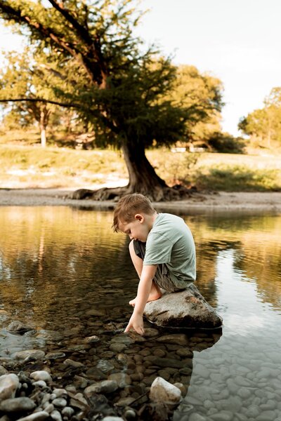 Little boy sitting on a rock at the pond