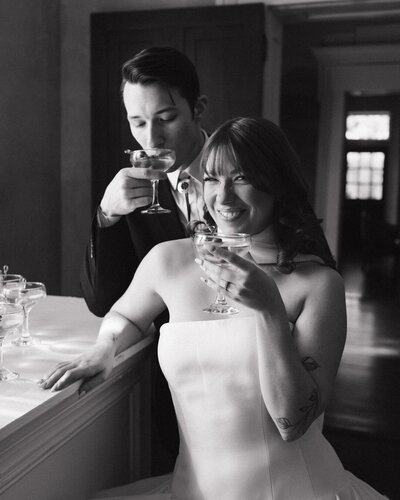 A bride and groom smile at the camera enjoying their martini at Riverwood Mansion wedding venue in Tennessee. Photo by Jaimee Tennant, a Nashville Wedding Photographer.