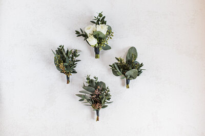 This elegant image highlights the groom's boutonniere alongside three others, meticulously crafted for the groomsmen. The attention to detail in each floral piece sets a sophisticated tone for the wedding, blending seamlessly with the day's overall aesthetic.