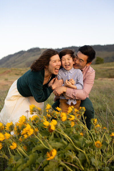 Candid Portland family photography of parents hugging their son in a wildflower field at sunset.