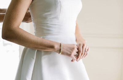 Bride getting fastened by mom at private residence, clasping her hands in front nervously looking out window. Photo taken by Chicago + Atlanta Photographer Ella Grace Richards of Forever Love Photography 