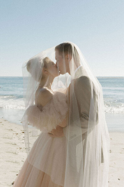 Coastal elopement in Carmel, CA. Couple in wedding attire kissing in front of the water.