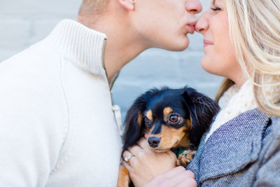couple shares a cute kiss on the nose during an engagement session while holding their dog.