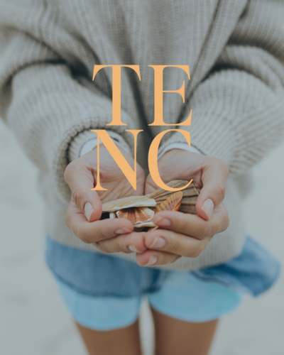 A person in a sweater and shorts holds seashells in their cupped hands. The letters "TENC" are overlaid in large orange font, evoking the playful energy of Sweet Pea Ink Creative, a web design and brand strategist studio.