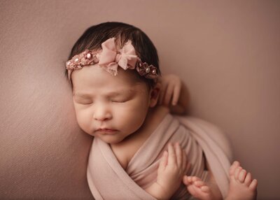 Baby sleeping on rose gold blanket with coordinating wrap and headband with pearl accents.