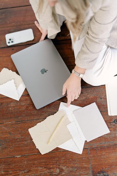 A woman sitting on the ground with a laptop and paper surrounding her.