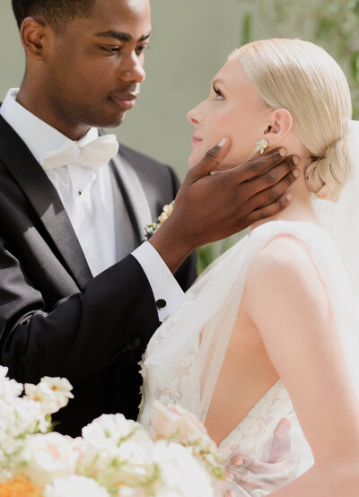 multicultural couple with black groom and white bride looking chic. groom touches brides face lovingly on a summers day.