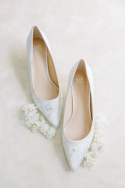 White shoes with bows on the toe surrounded by white flowers