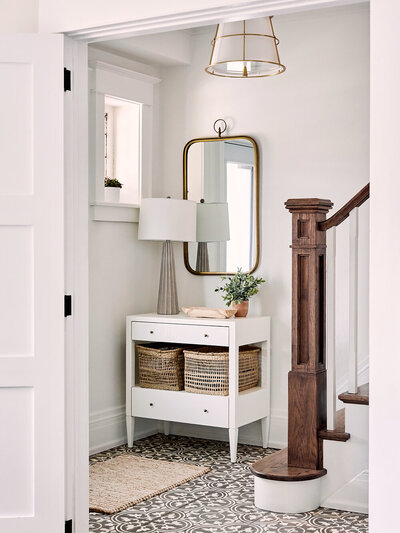 small foyer with patterned tile wood newel post white walls entry table concrete lamp gold mirror and good light fixture