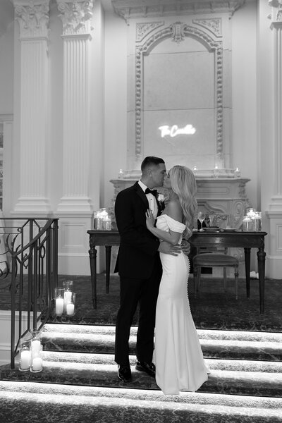 Couple wearing wedding attire and holding white flowers standing at steps in city hall