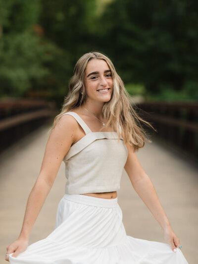 high school senior graduate in white dress twirling at park for senior photos