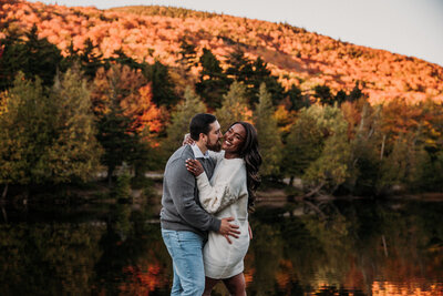 man and woman embracing and smiling while standing next to a lake