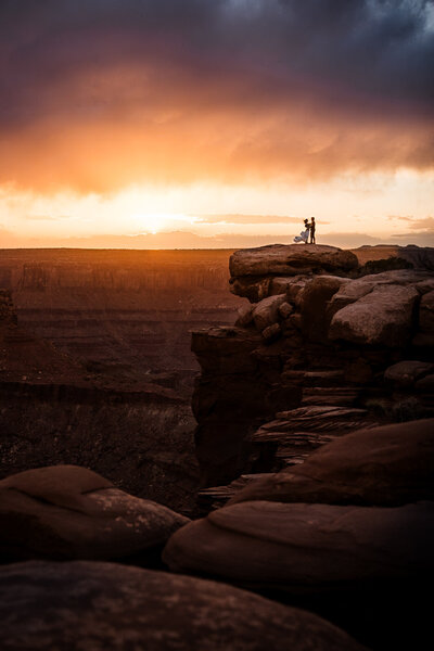 having just eloped, a couple sitting on joshua tree boulders snuggle in close and smile.