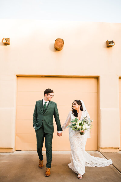bride and groom holding hands in front of adobe style house