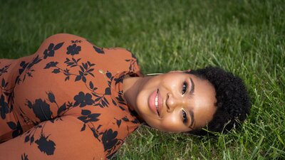 Teen girl lays on grass and smiles into the camera.
