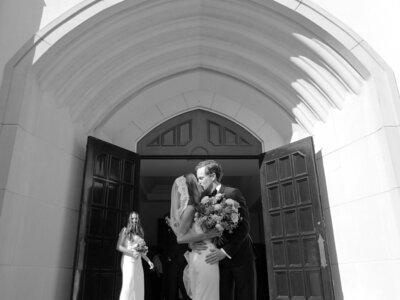 Brid enad groom walking close to each other and smiling while wedding party walks behind them