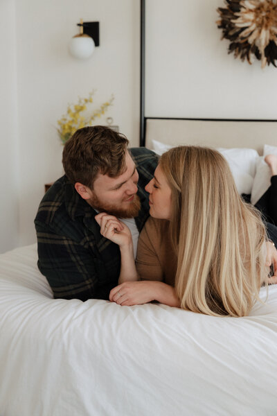 A couple sharing an intimate, playful moment on a cozy bed in a bright, warm setting.