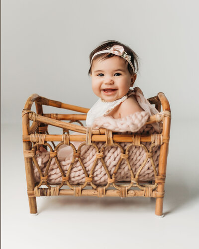 photo of baby sitting in basket wearing a baby romper and floral headband