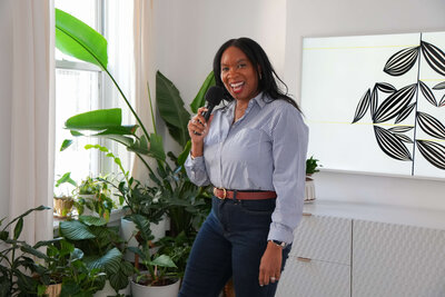 confident-business-woman-jacinta-holding-microphone-standing-near-green-plants-during-event