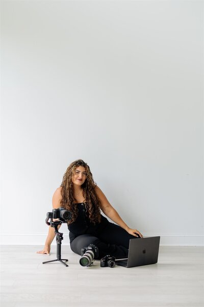 Hiba, Raleigh wedding photographer and videographer, smiling behind her desk with camera equipment during a personal branding photo session.