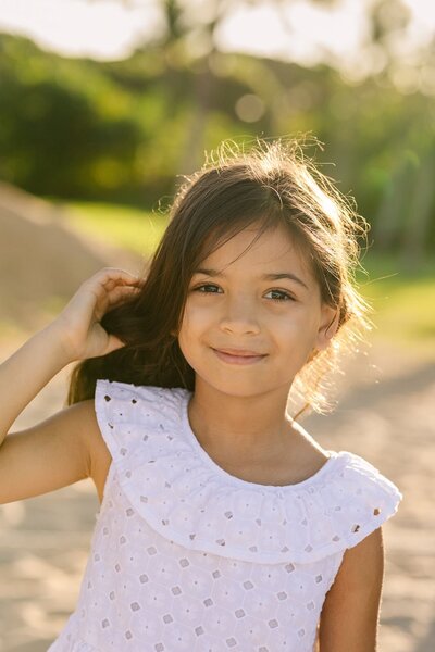 A little girl holds her hair smiling at the camera.