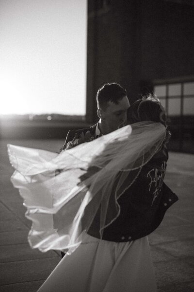 A couple kisses outdoors at sunset, the wind blowing the bride's veil. Both are wearing detailed jackets, highlighted perfectly through our Showit template customization for wedding planners.