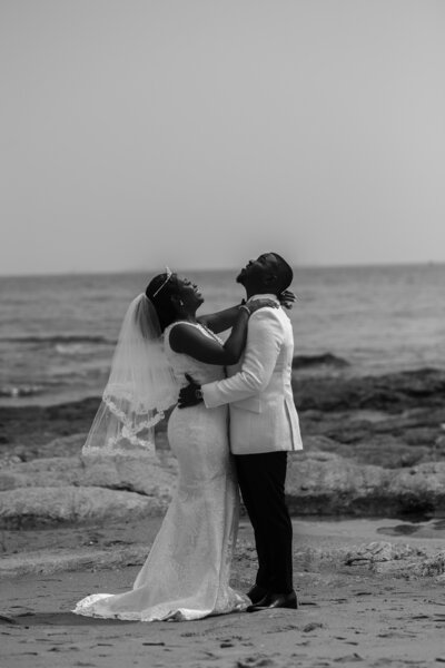 A bride and groom with their arms around each other on the edge of the water