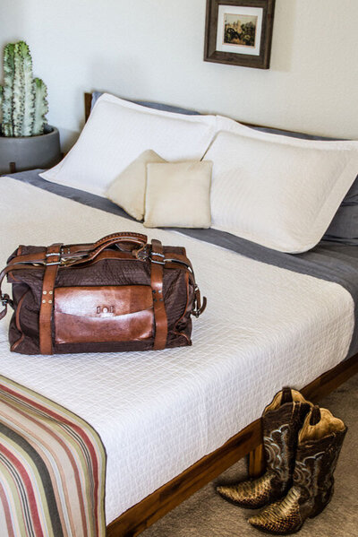 Location branding photo Gatos Trail bedroom bed with vintage suitcase cowboy boots next to it