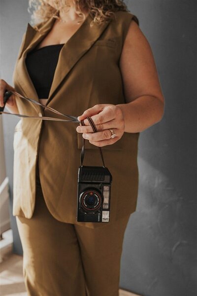 Andrea Cakmar holds a vintage camera by the strap, partially visible against a dark background.