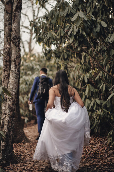 Eloping couple hiking through the forest along a trail