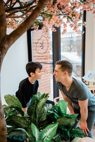 Dr. Michael Rabinowitz, of Little Chompers, smiles and introduces himself to his young patient. Office greenery and a blooming floral tree frame the photo in the foreground. In the background you can see a hint of Andersonville, Chicago's historic Clark Street (including a local Starbucks Coffee).