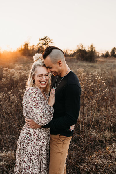 Couple laughing together in a field at sunset.