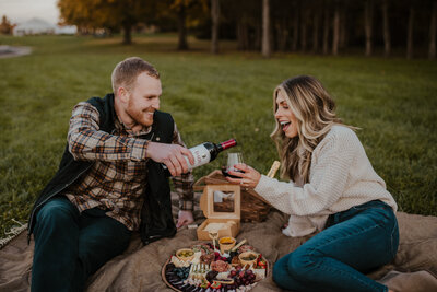 Couple enjoys sips of wine and eating charcuterie during their engagement session.