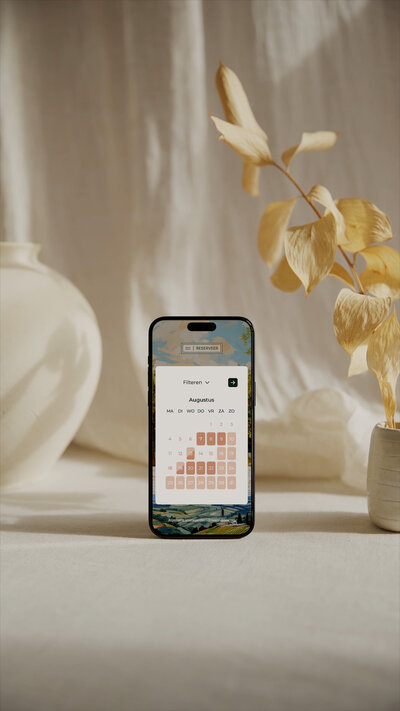 Mobiele telefoon met reserveringskalender voor augustus, gestyled met zachte beige tinten en natuurlijke elementen