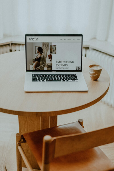 Laptop sitting on light wood table with a website mockup showing on screen