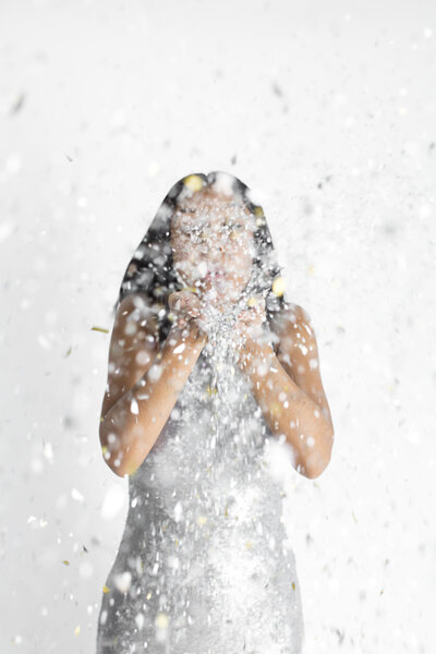 brunette woman wearing a silver dress blowing silver confetti everywhere with confetti obscuring her face