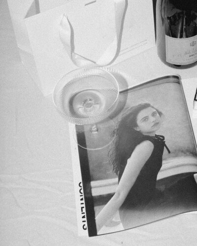 Black and white photo of a magazine with a woman's portrait, a glass dish, a ribbon, and a wine bottle on a table—an elegant scene where you could plan to hire an online business manager for efficient services.