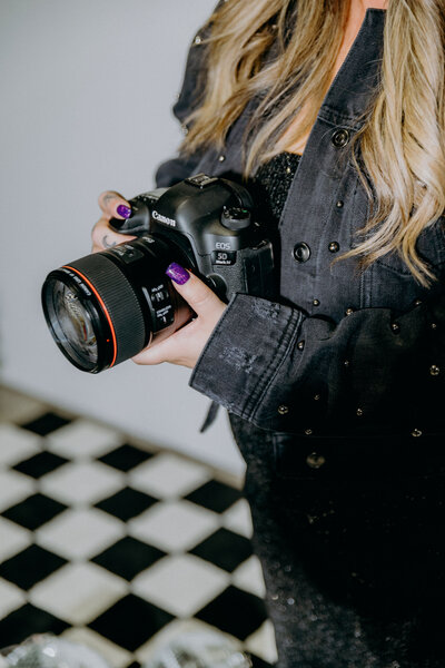 A woman capturing moments with a camera in an Austin photo studio, against a checkered floor backdrop.