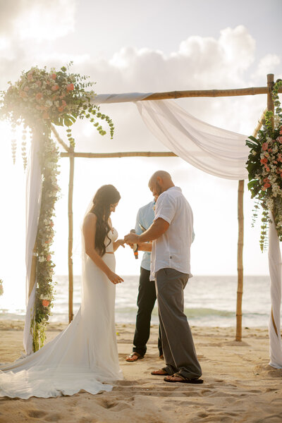bride and groom exchanging rings during their ceremony on the beach
