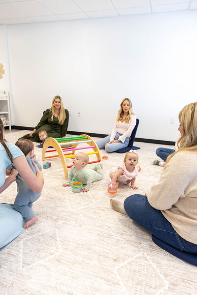Group of babies playing in a circle while their moms watch