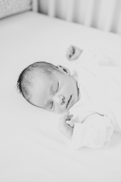 Black and white image of newborn baby girl sleeping in crib during newborn photography session in Raleigh NC