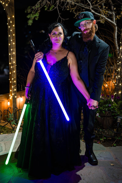 Bride and groom holding glowing lightsabers during their Star Wars–themed wedding at Christies of Genesee in Colorado.