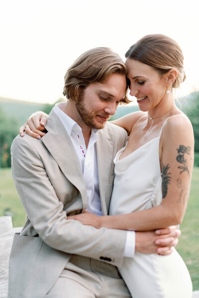 Bride and groom embrace in chic vermont wedding in alexandra grecco slip dress and tattoos showing