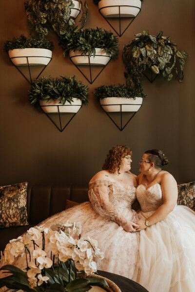 A newlywed couple sitting on a couch together holding hands 