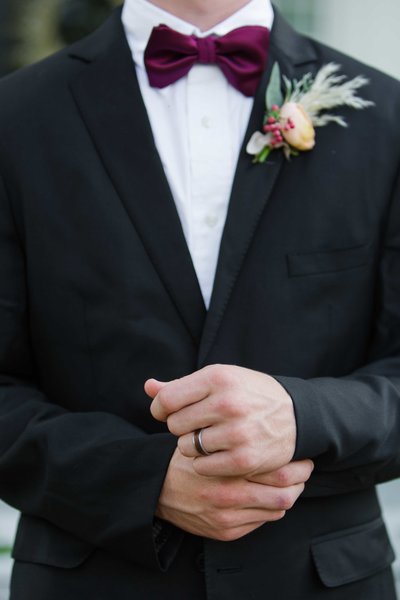 Groom adjusting buttons showing his ring, bowtie and boutonniere