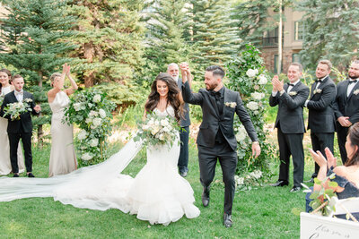 A bride and groom hold hands and cheer as they walk down the aisle after their wedding ceremony in Vail Colorado.